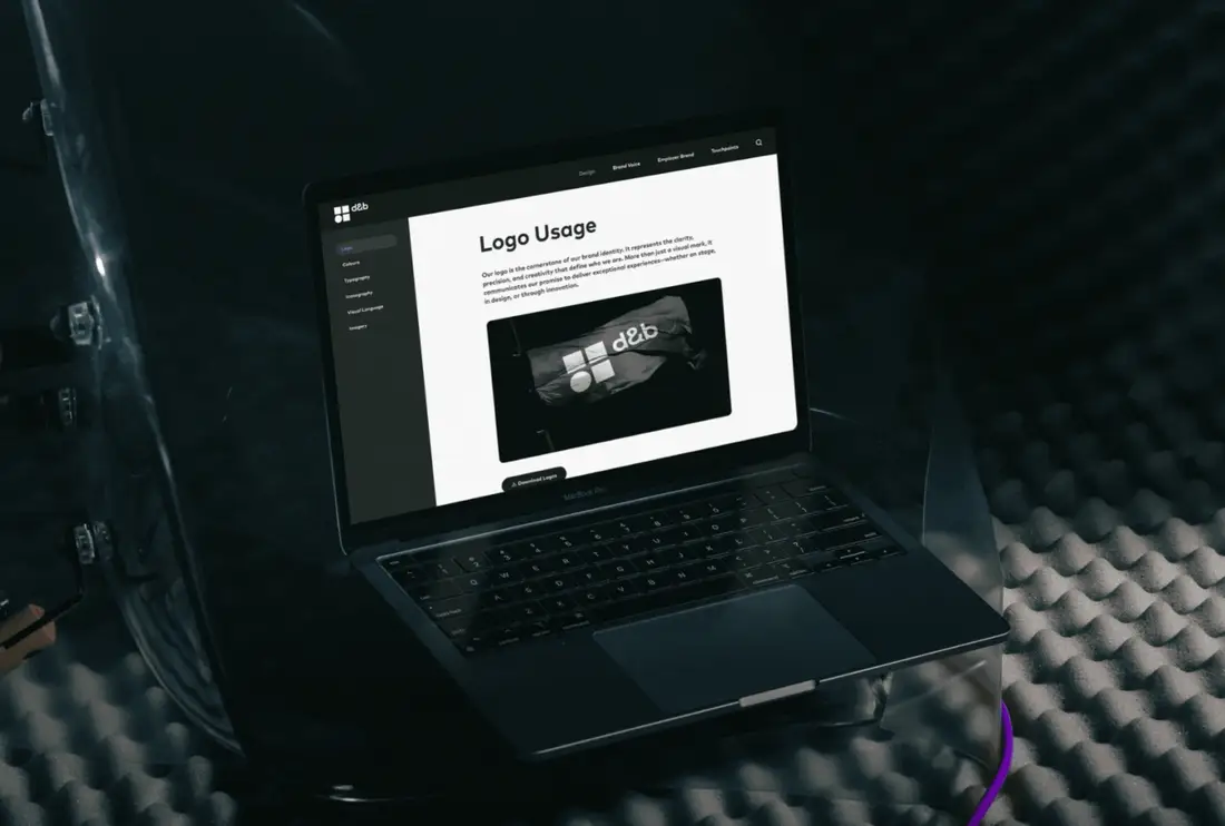Laptop auf akustischem Schaumstoff, auf dem Bildschirm der Online-Style-Guide der d&b group mit dem Kapitel „Logo Usage“ und einer Abbildung des Logos auf schwarzem Stoff.