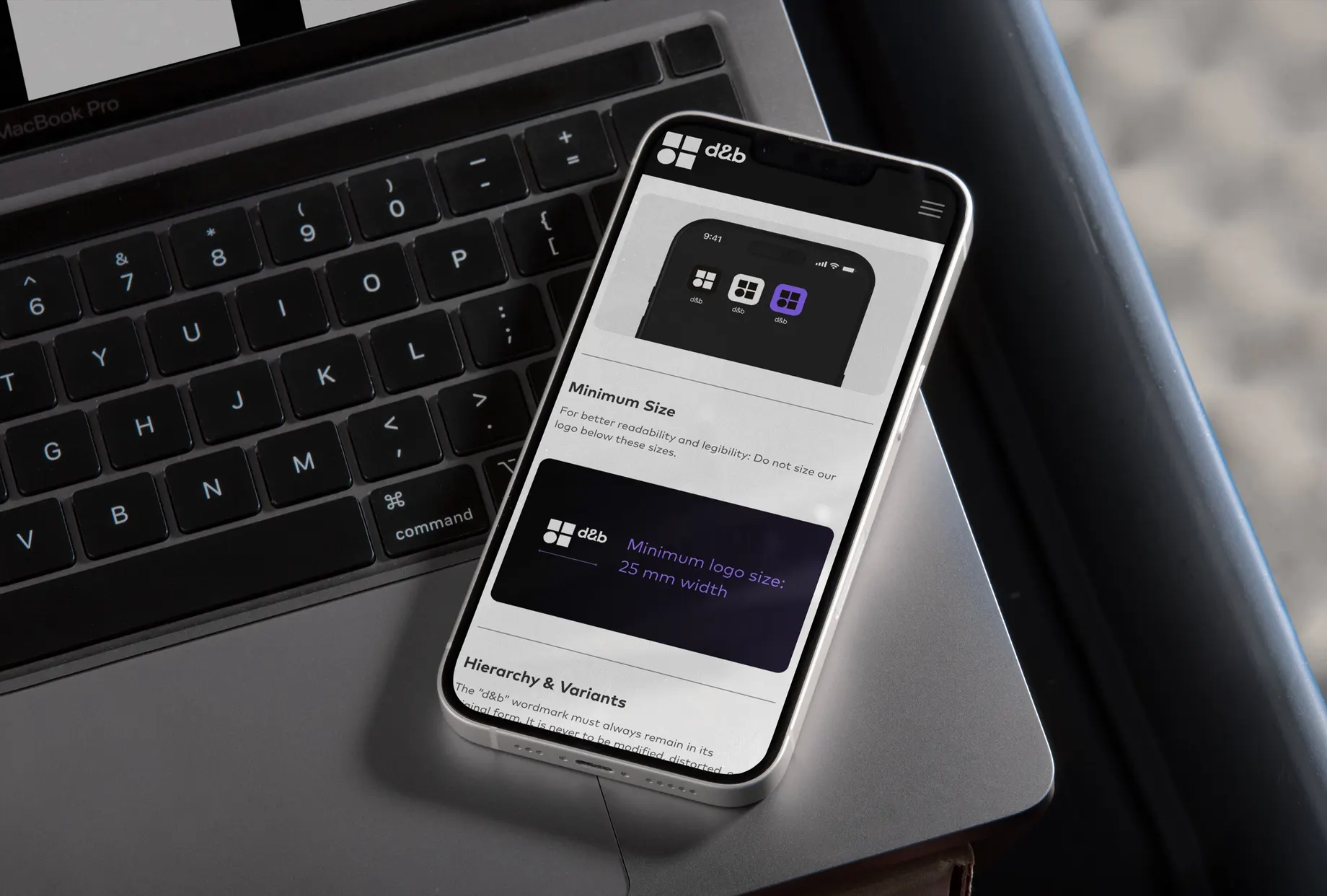 Smartphone auf einem MacBook, auf dem Bildschirm der Style-Guide mit den Kapiteln „Minimum Size“ und „Hierarchy & Variants“ — dazu die Vorgabe, das Logo nicht kleiner als 25 mm Breite zu setzen.