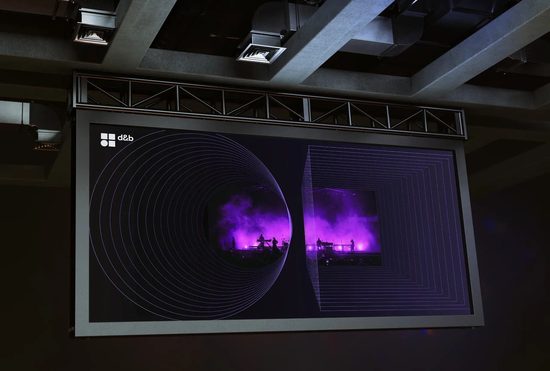 Grosse Leinwand in einem Saal mit Betondecke. Darauf zwei Bühnenaufnahmen in violettem Licht, gerahmt von konzentrischen Kreisen und Quadraten — Bildsprache für Schallausbreitung.