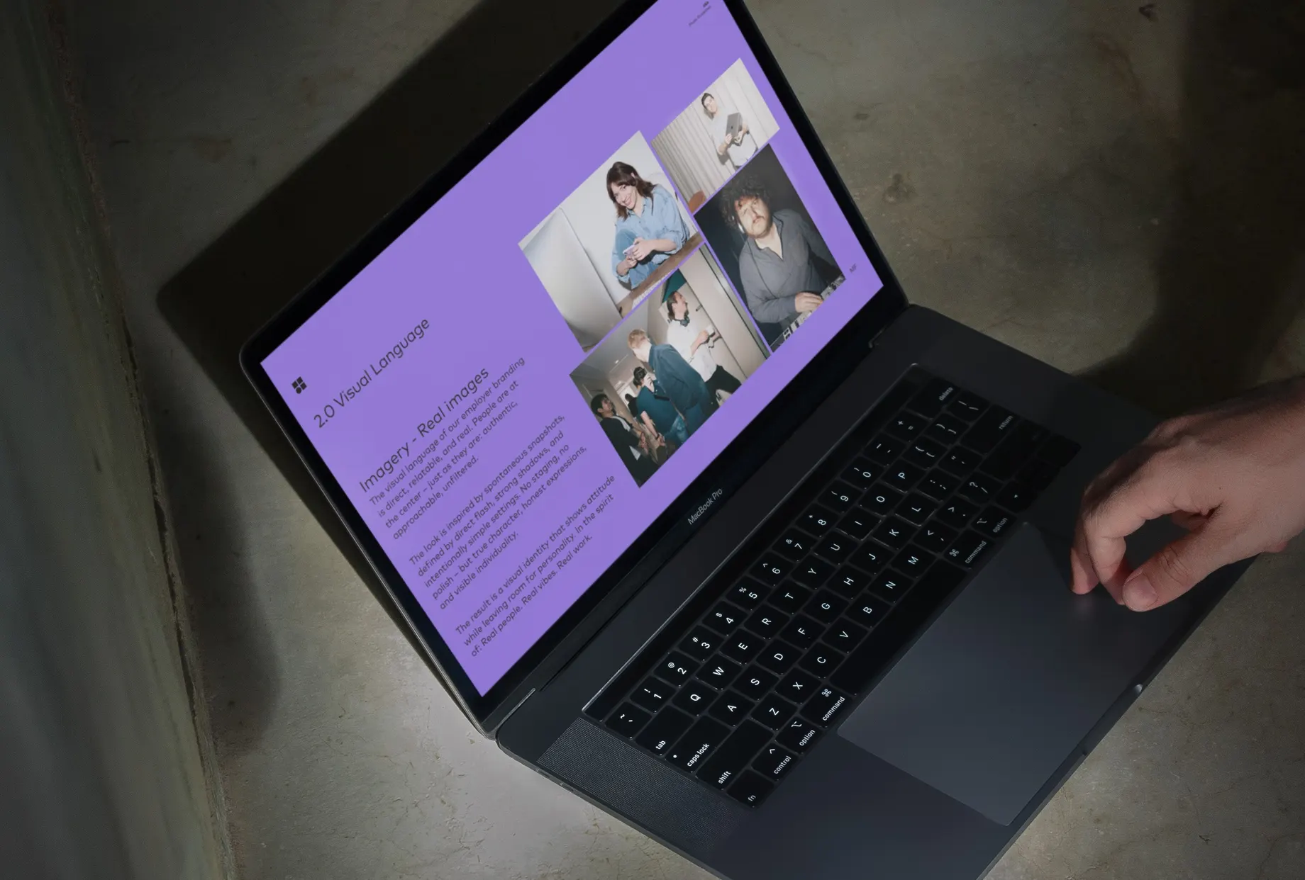 Laptop auf einem Betonboden, auf dem violetten Bildschirm das Kapitel „2.0 Visual Language – Imagery, Real images“ mit einer Collage aus vier Mitarbeiteraufnahmen.