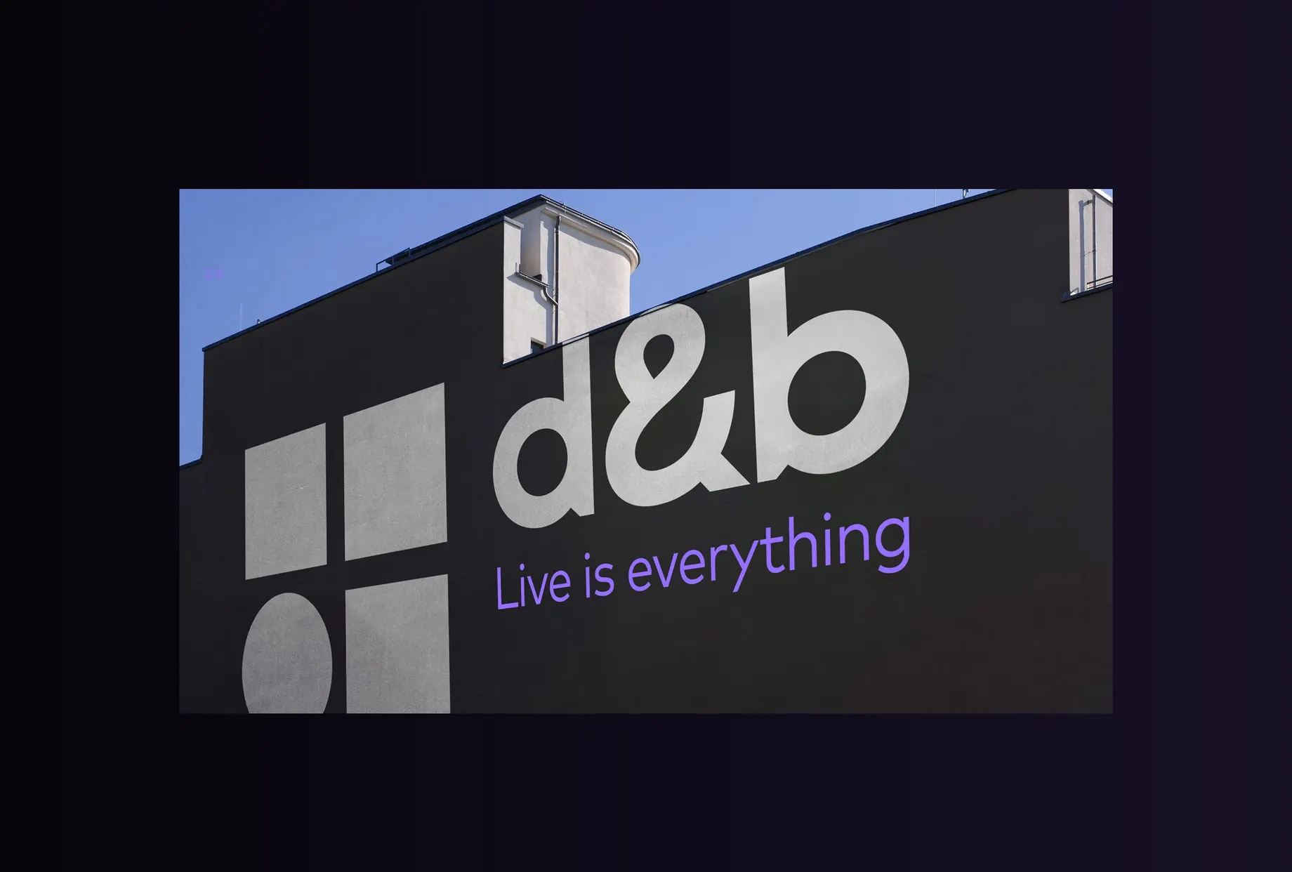 Gebäudefassade mit grossem d&b-Logo und dem Claim „Live is everything“ vor blauem Himmel.
