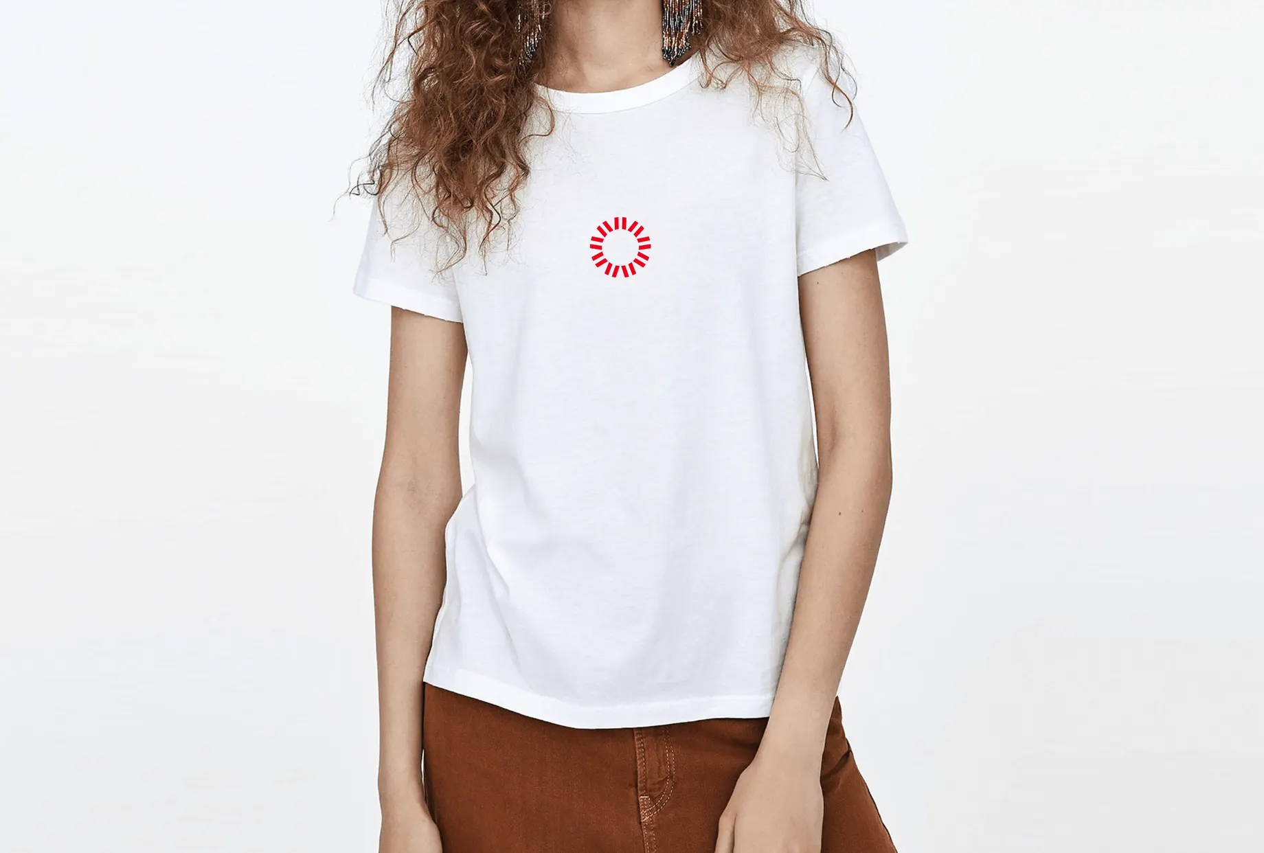 Person in weissem T-Shirt mit dem kleinen roten Strahlenkreis auf der Brust vor hellem Hintergrund.