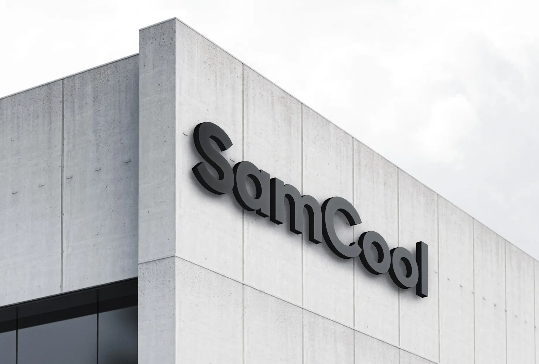 Betonfassade eines Gebäudes mit dem plastisch aufgesetzten SamCool-Schriftzug in Dunkelgrau, darüber bedeckter Himmel.