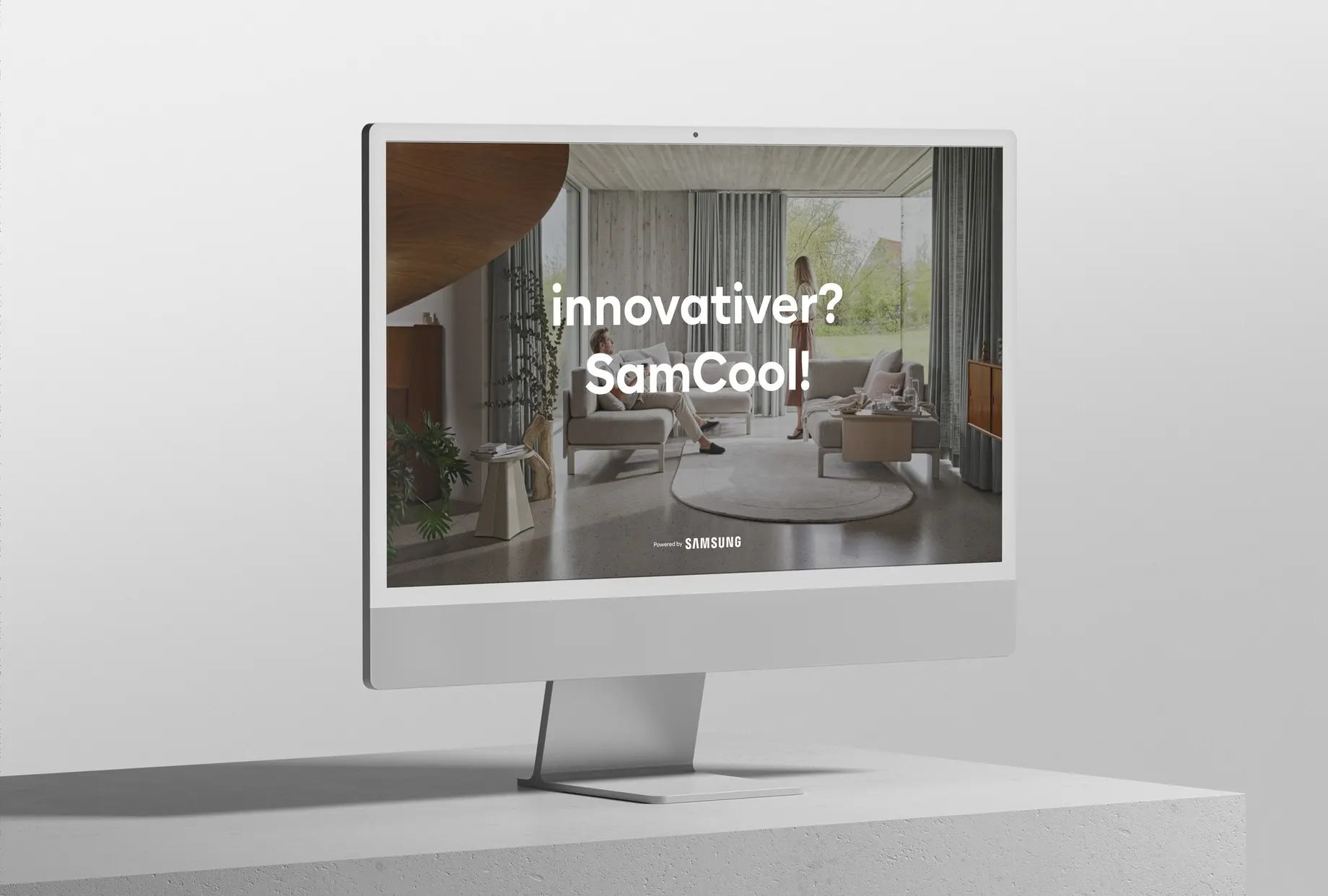 Bildschirm auf einem hellen Sockel, darauf ein Wohnraum mit bodentiefen Fenstern und die Zeile „innovativer? SamCool!“ über dem Hinweis „Powered by Samsung“.