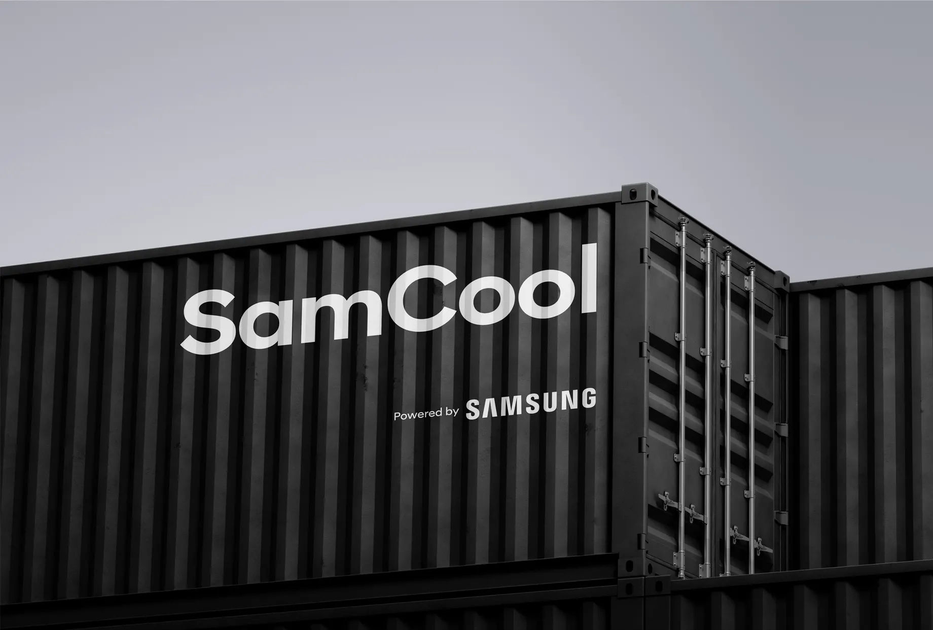 Dunkler Überseecontainer vor grauem Himmel, beschriftet mit dem SamCool-Schriftzug und „Powered by Samsung“.