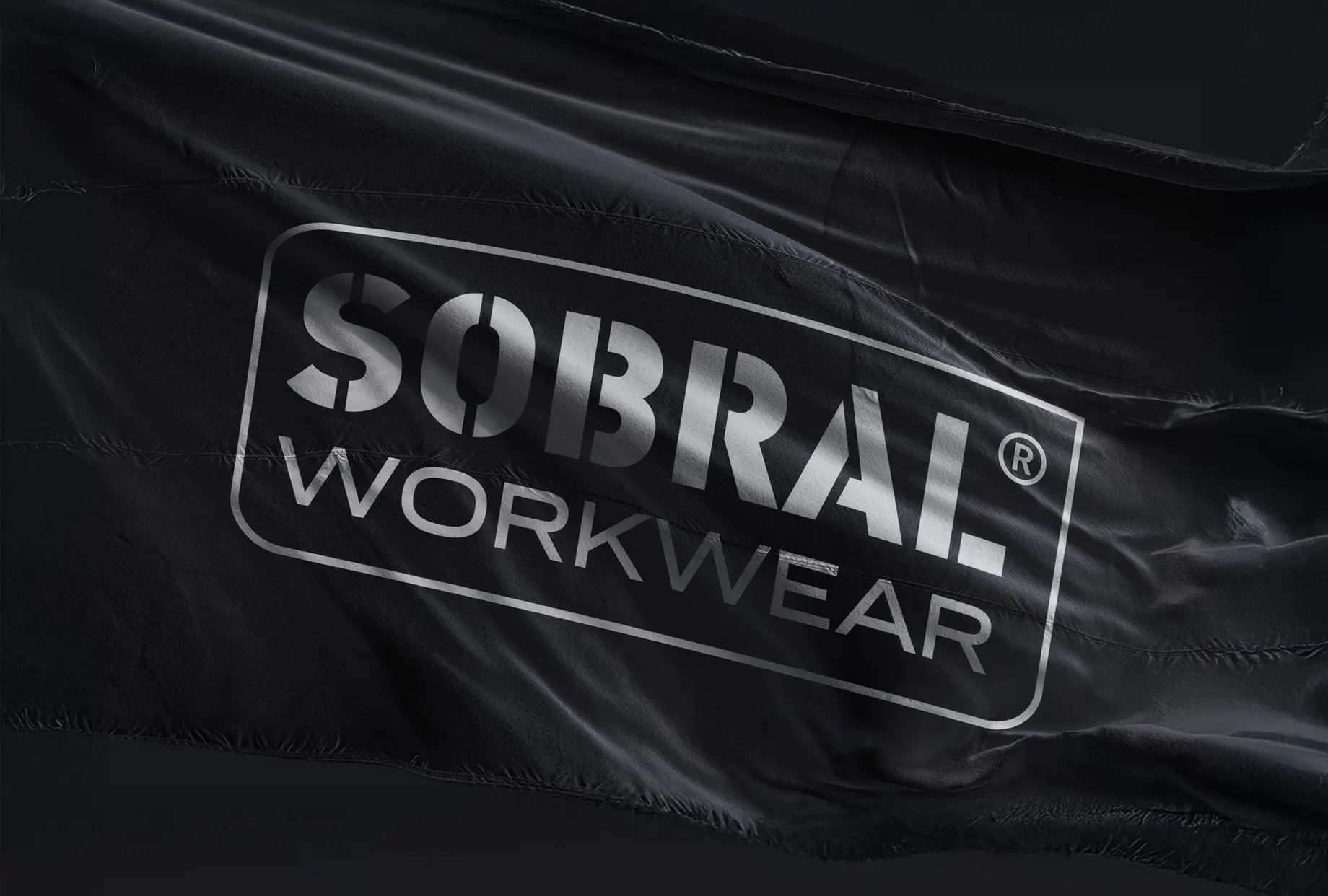 Wehende schwarze Fahne mit dem gerahmten Logo „Sobral Workwear“ in Silber, im Streiflicht aufgenommen.