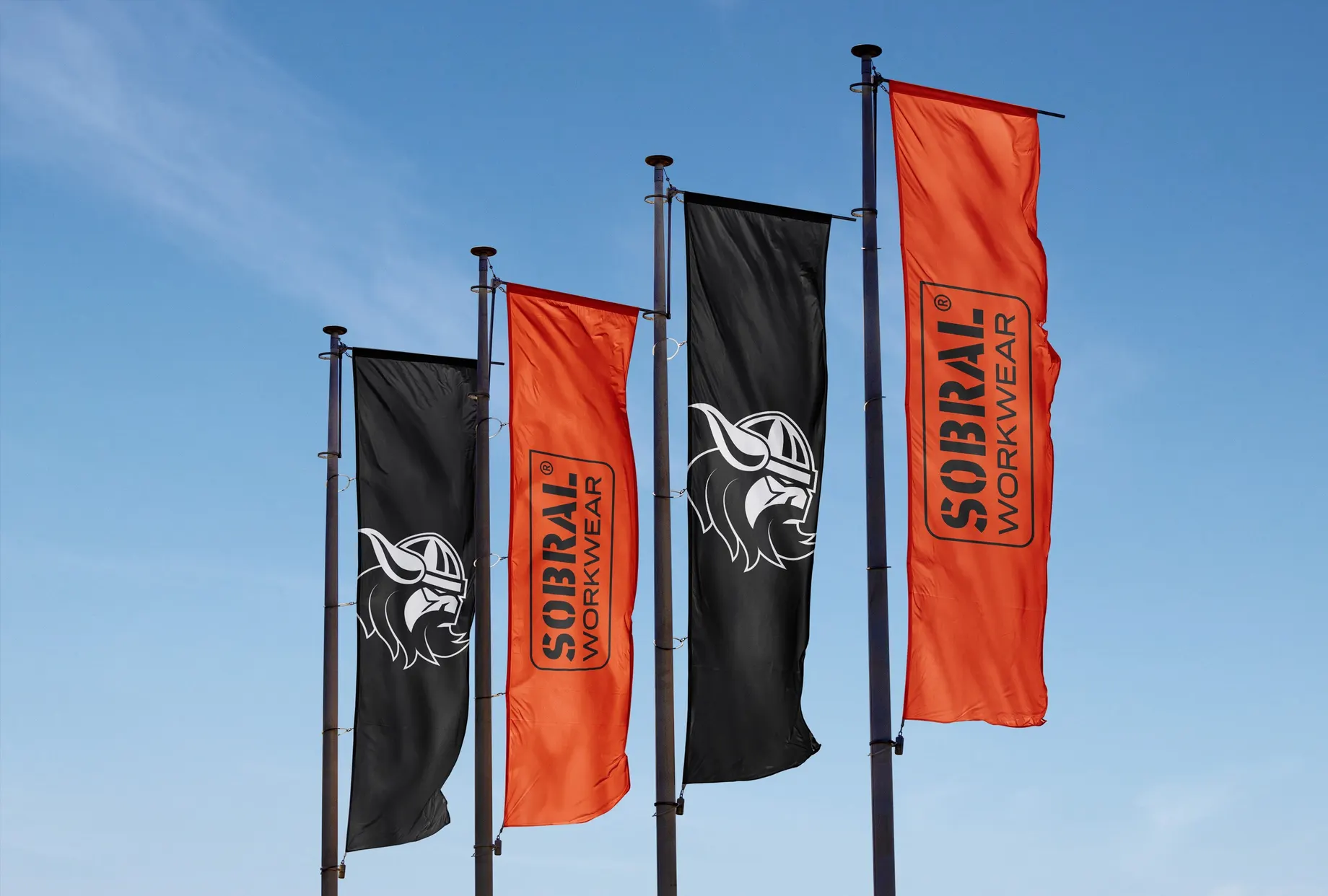Vier Hochformatfahnen an Masten vor blauem Himmel: abwechselnd schwarz mit dem Wikingerkopf als Bildmarke und orange mit dem Schriftzug „Sobral Workwear“.