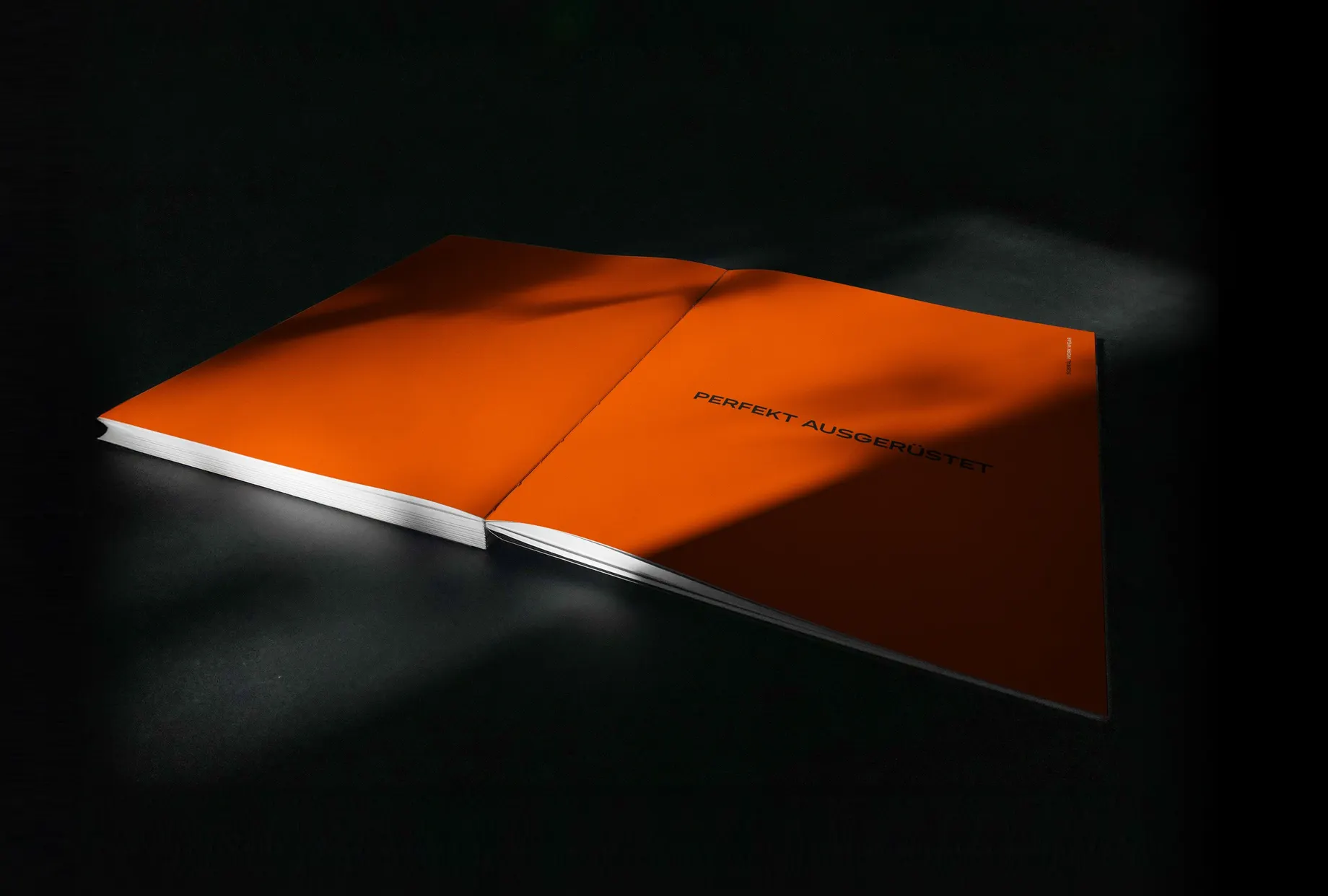 Aufgeschlagener Katalog mit leuchtend orangen Seiten auf dunklem Grund, auf der rechten Seite die Zeile „Perfekt ausgerüstet“.