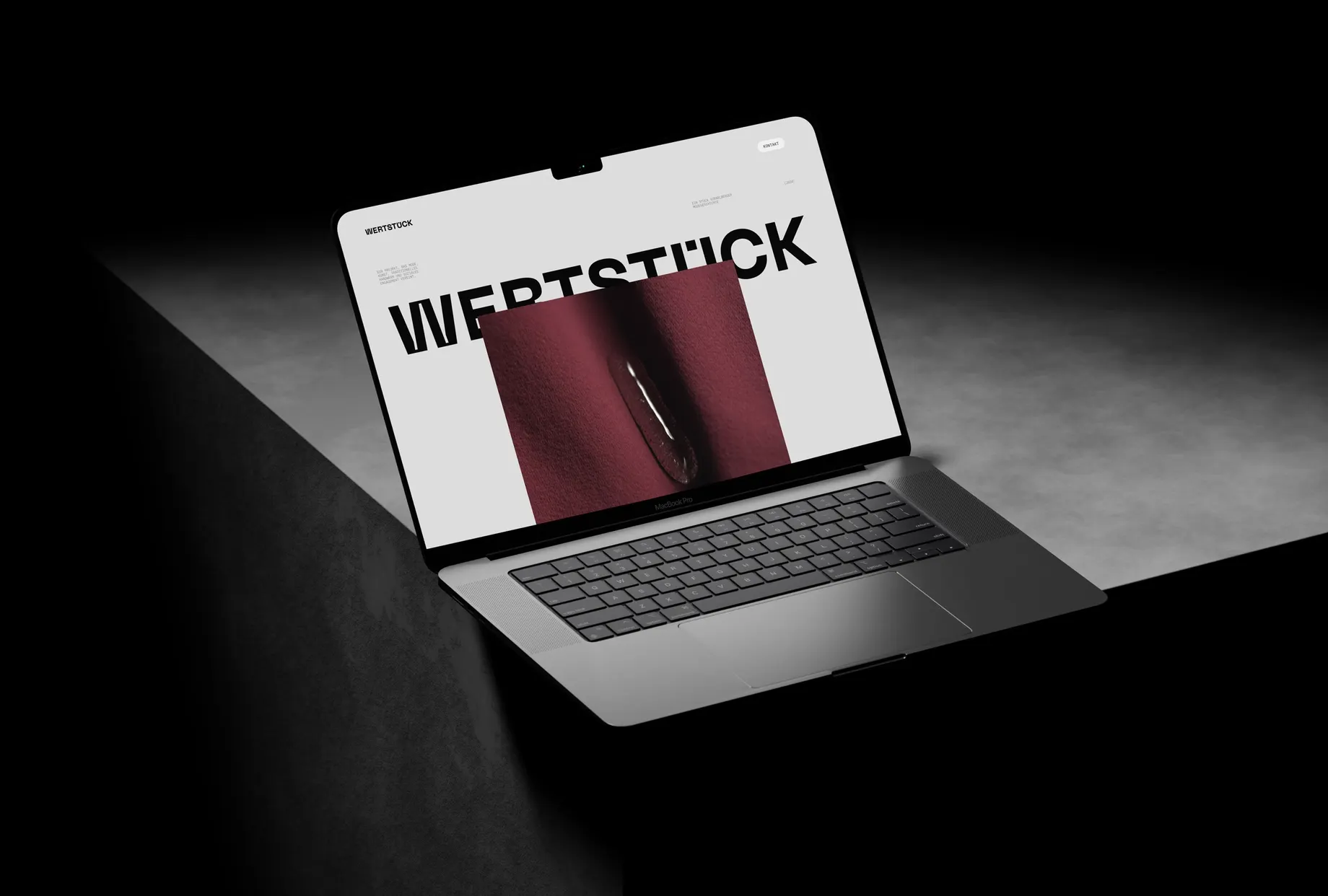 Laptop im Spotlicht, auf dem Bildschirm die Wertstück-Website: grosser Schriftzug über einer Detailaufnahme von dunkelrotem Stoff mit Reissverschluss.